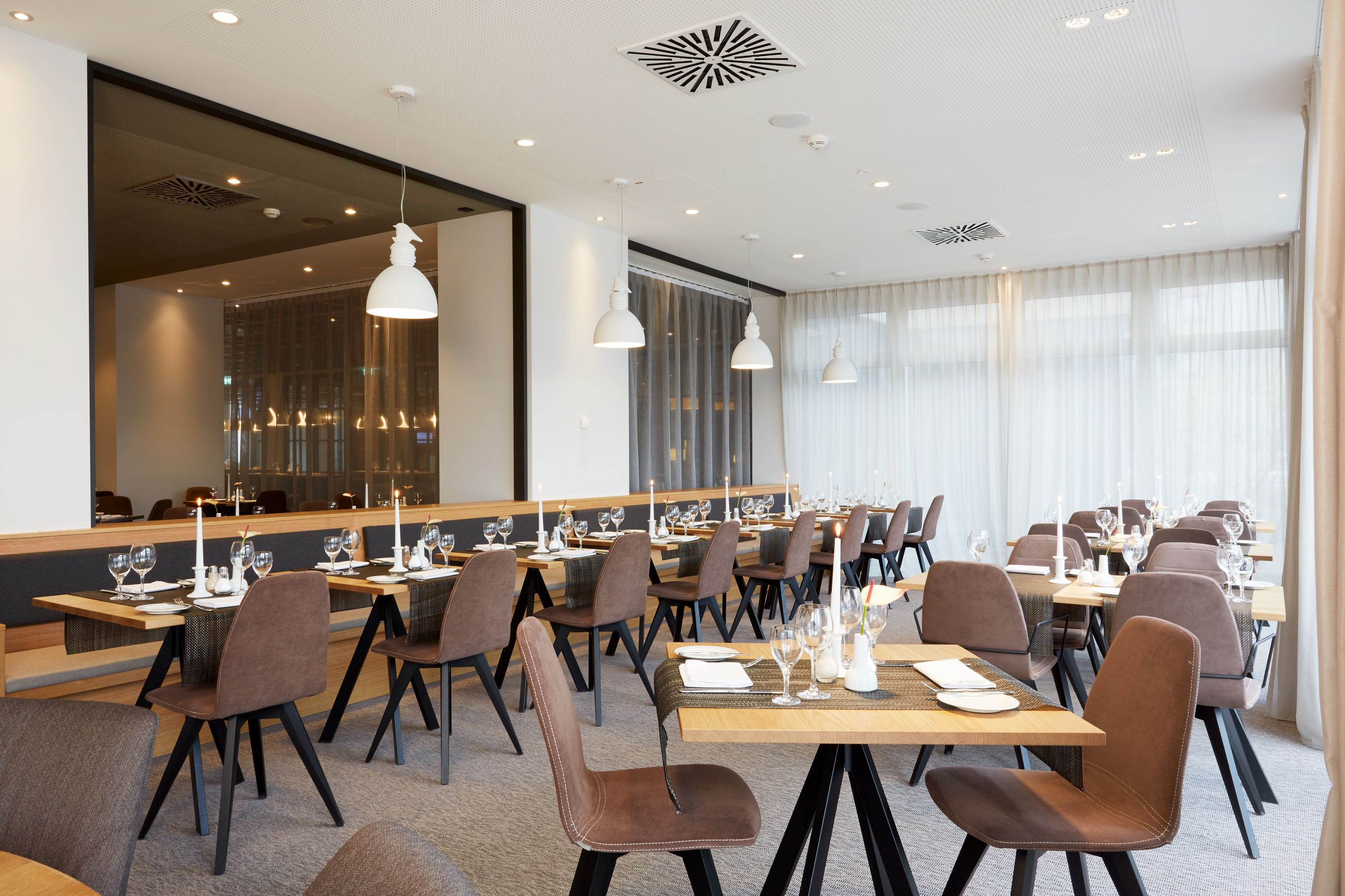 A modern dining area with multiple tables set for a meal, featuring contemporary chairs and overhead lighting.
