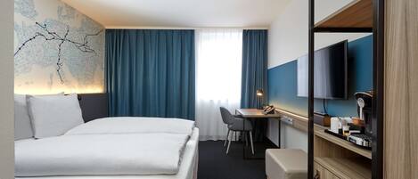 Una habitación de hotel con cama, escritorio, silla, televisor y un mapa en la pared.