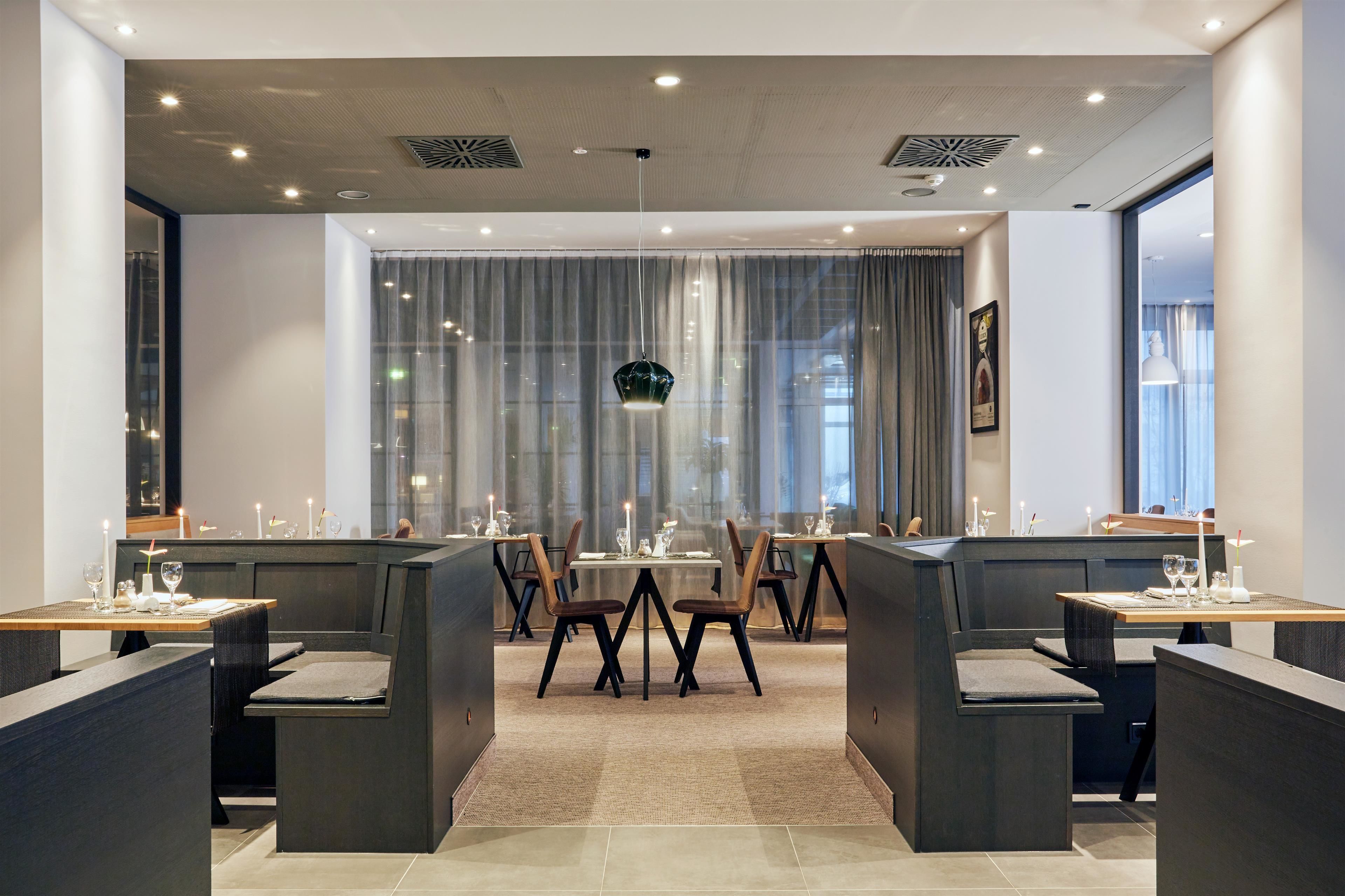 Un comedor moderno con mesas altas, cabinas y ventanas amplias con cortinas, además de iluminación empotrada en el techo.