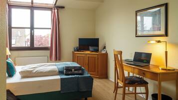 A hotel room with a bed, a desk with a laptop, a television, and a window with curtains.