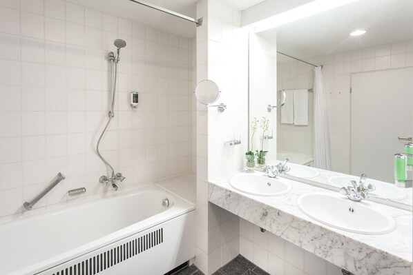 A modern bathroom with a bathtub, two sinks, and a large mirror.