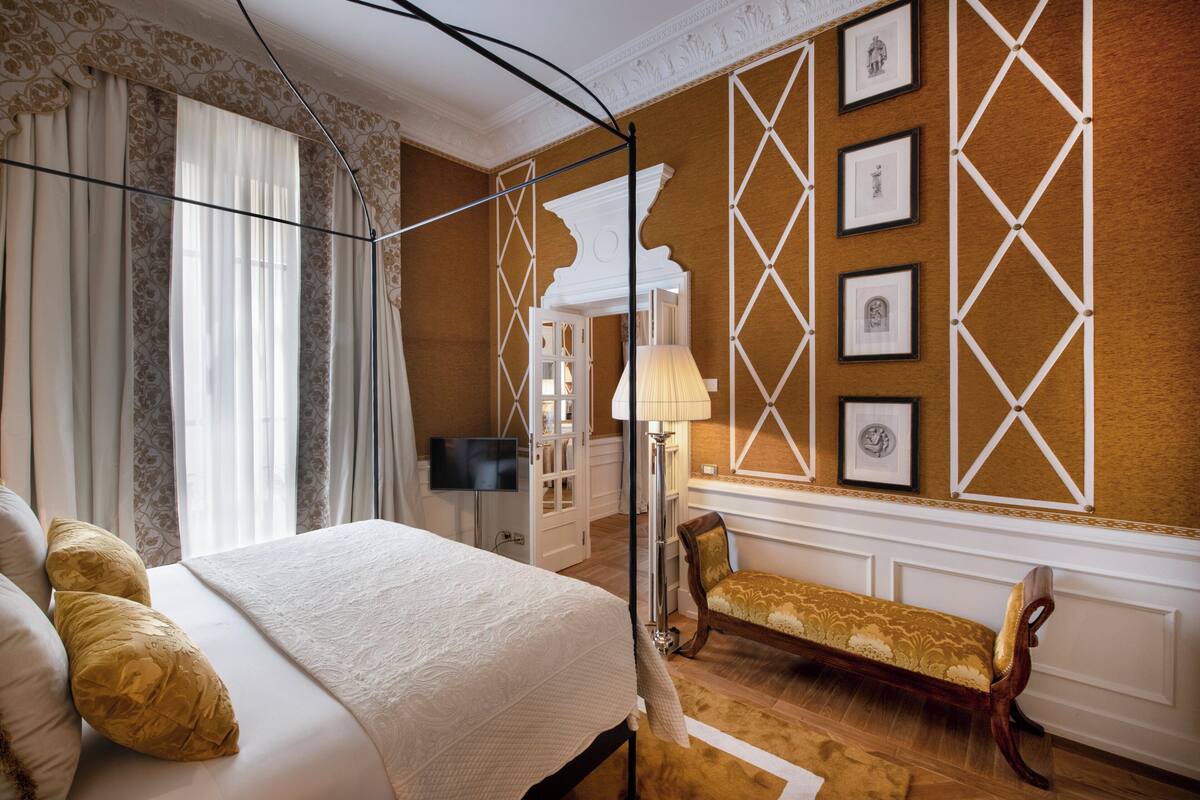 A hotel room with a large bed, a bench, a TV, and framed pictures on the wall.