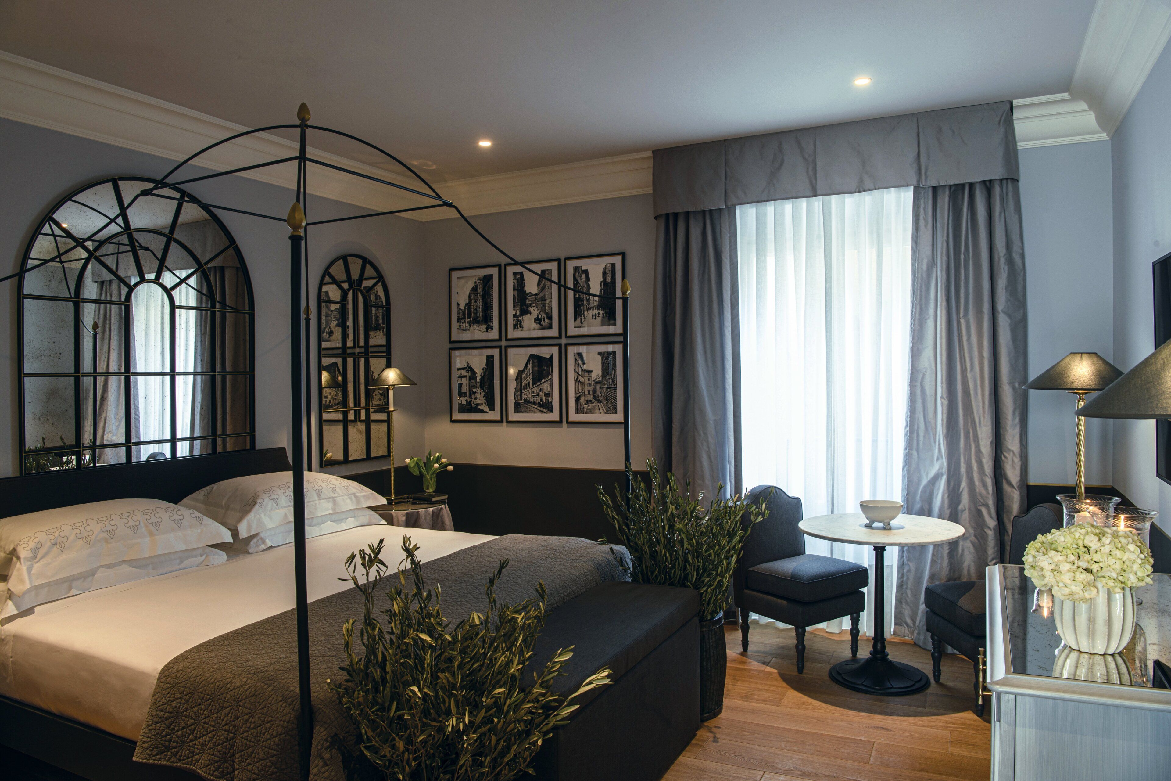 Une chambre moderne avec un grand lit, une table de chevet, une chaise et une petite table sur laquelle est posé un vase de fleurs.