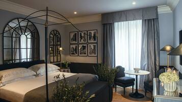 Une chambre moderne avec un grand lit, une table de chevet, une chaise et une petite table sur laquelle est posé un vase de fleurs.