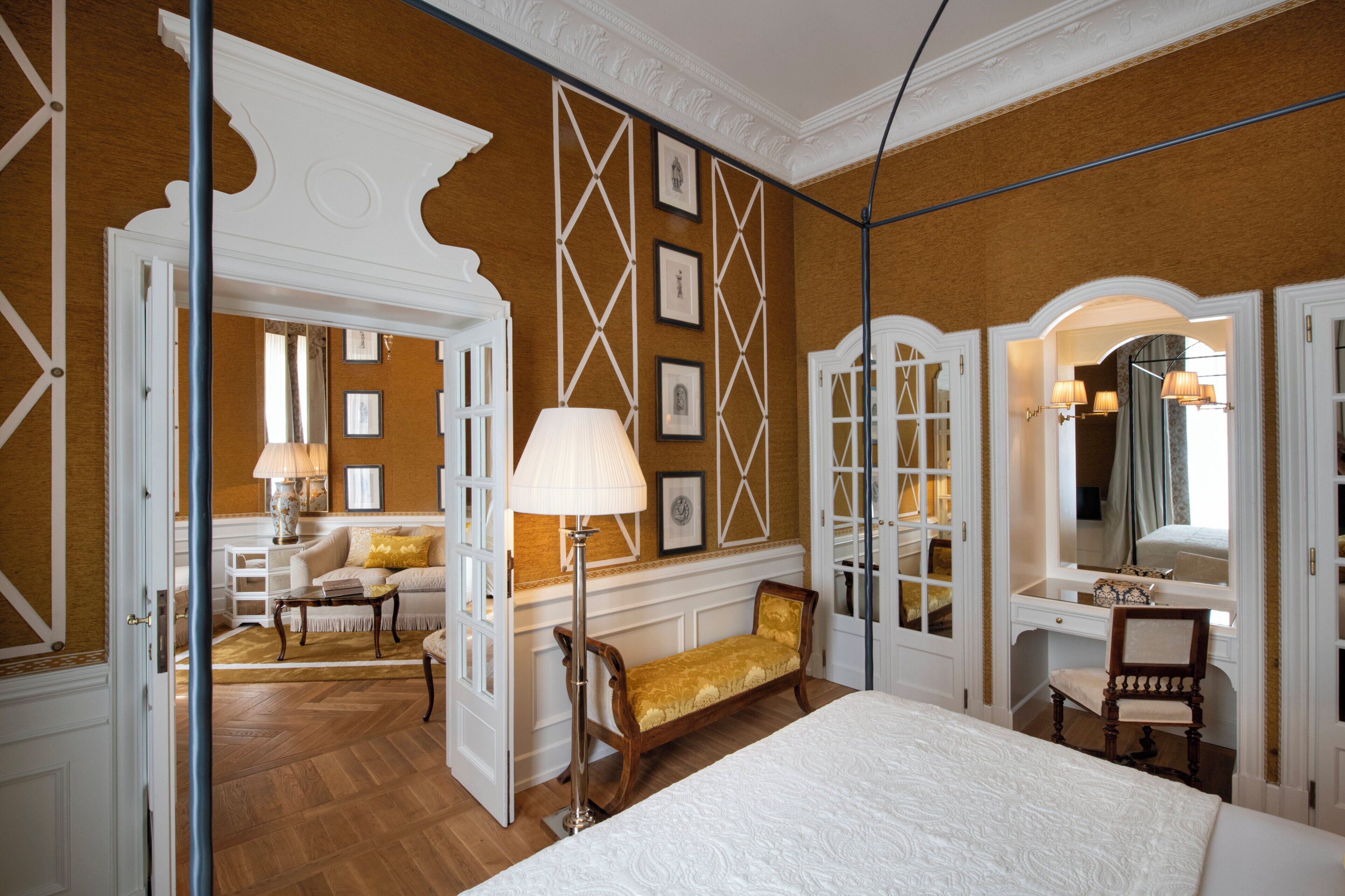 A hotel room with a large bed, a sitting area with a bench, a desk, and a mirror.