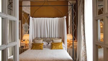 A bedroom with a canopy bed, two bedside tables with lamps, and a view of the room through a window.