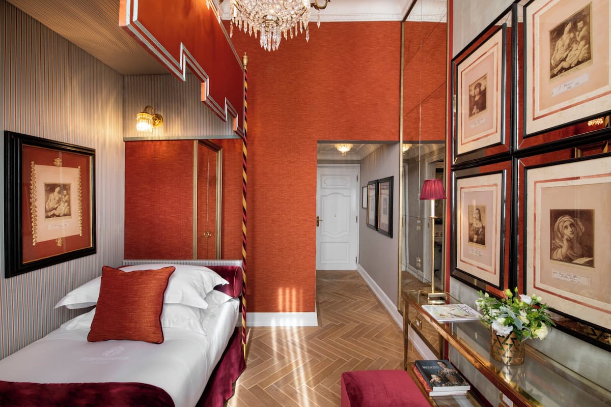 Habitación de hotel con cama, espejo, cuadros enmarcados y candelabro.