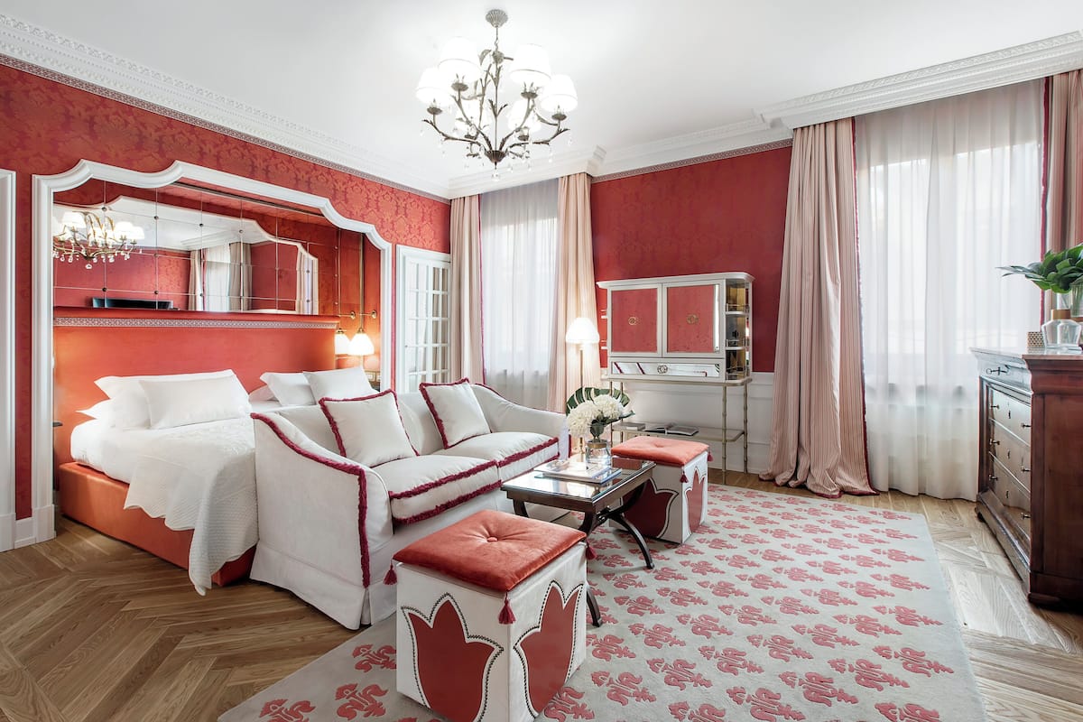 Una habitación con una decoración en tonos rojo y blanco, que incluye una cama, un sofá, una mesa de centro y un aparador.