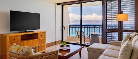 A living room with a flat-screen TV, wicker furniture, a sofa, a coffee table, and a view of the ocean through large sliding doors.
