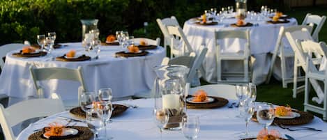 A series of round tables set up outdoors with white tablecloths, arranged in a semi-circle facing a scenic view of the ocean.
