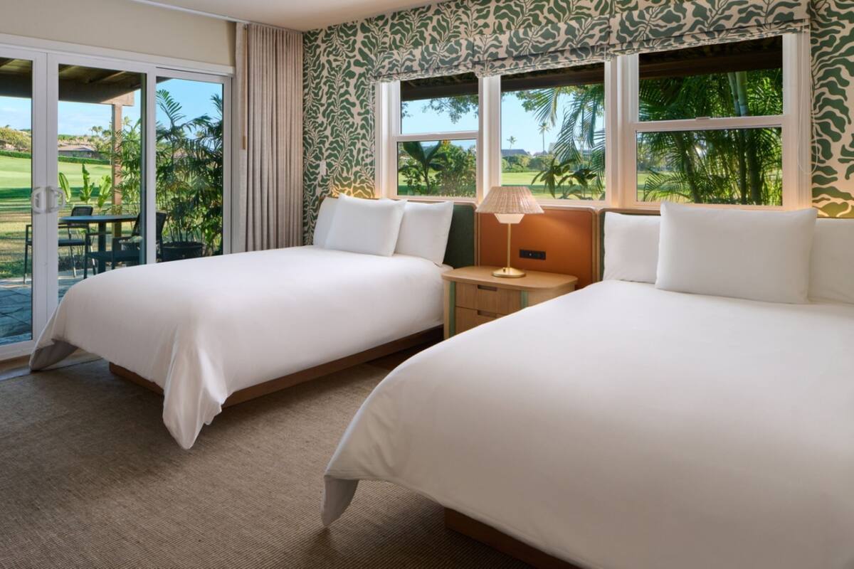 Habitación de hotel con dos camas, una mesita de noche con lámpara y vistas a un campo de golf por las ventanas.