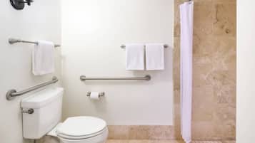 A bathroom with a toilet, grab bars, a shower curtain, and two towels on towel racks.