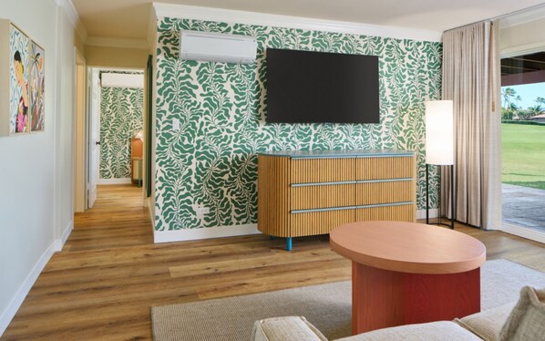 Una sala de estar moderna con piso de madera, una mesa redonda para café, un televisor montado en la pared y un papel tapiz estampado.