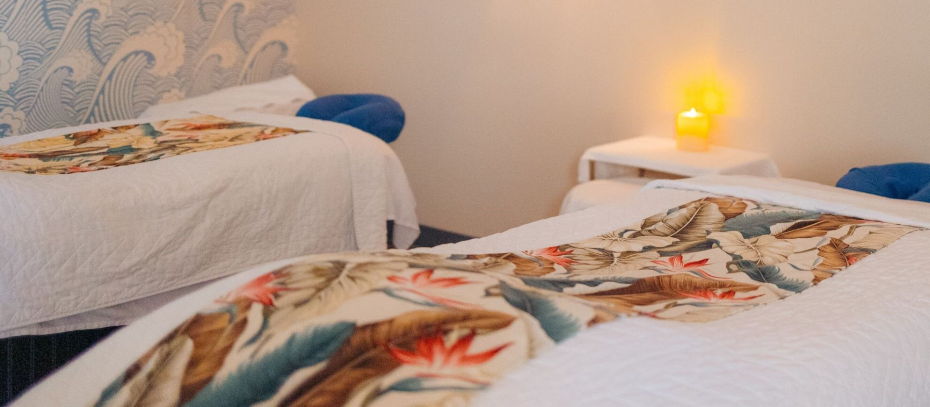 Habitación de hotel con dos camas, cada una con una colcha floral, una mesita de noche con una vela y un cabecero estampado.