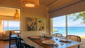 A dining area with a wooden table set for four, two chairs, and a view of the ocean. - Royal Lahaina Resort & Bungalows (Lahaina)