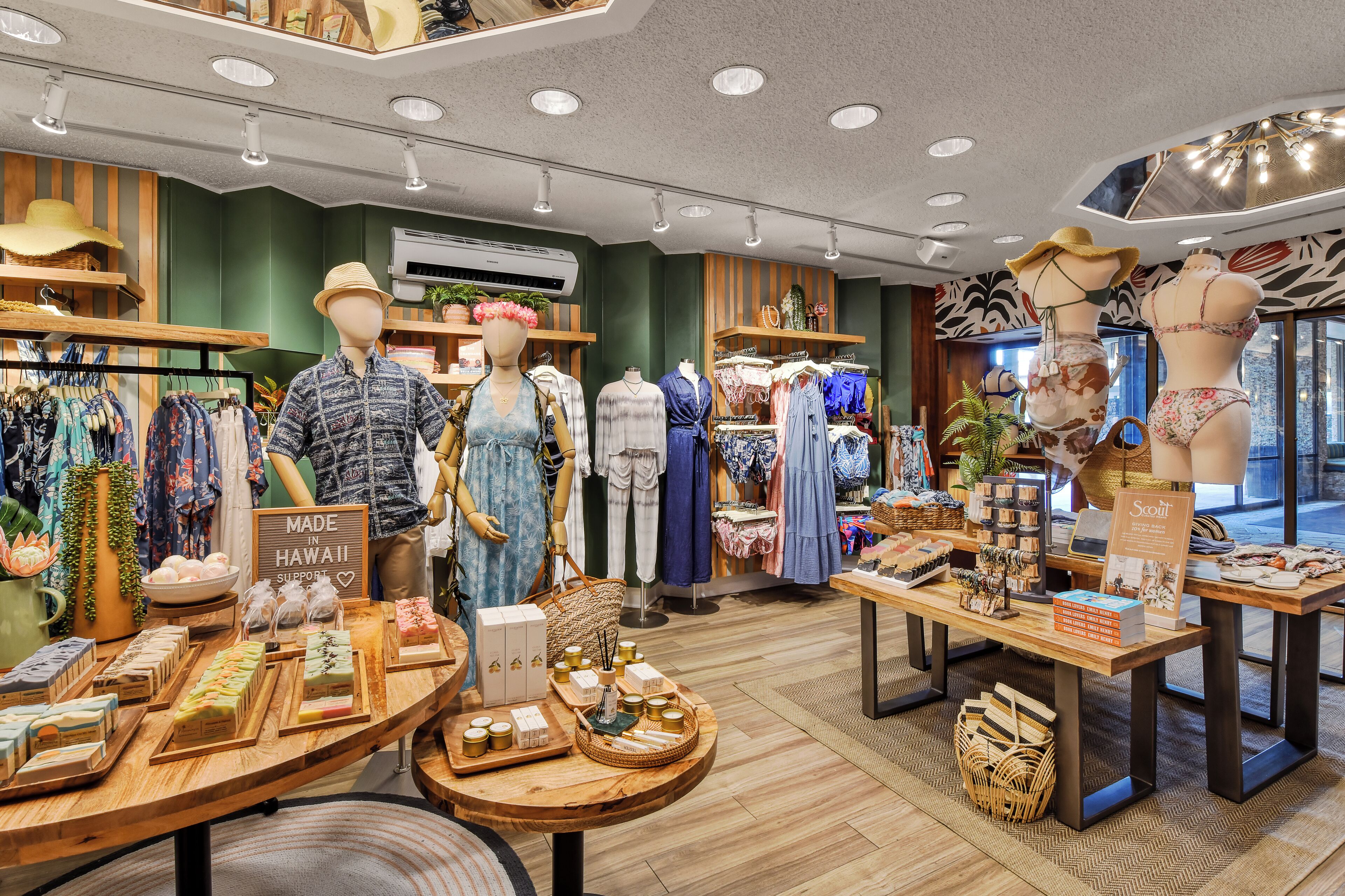 Un negozio di abbigliamento esclusivo con manichini che espongono i capi, un tavolo di legno con diversi prodotti e un'insegna che indica che il negozio è realizzato alle Hawaii.