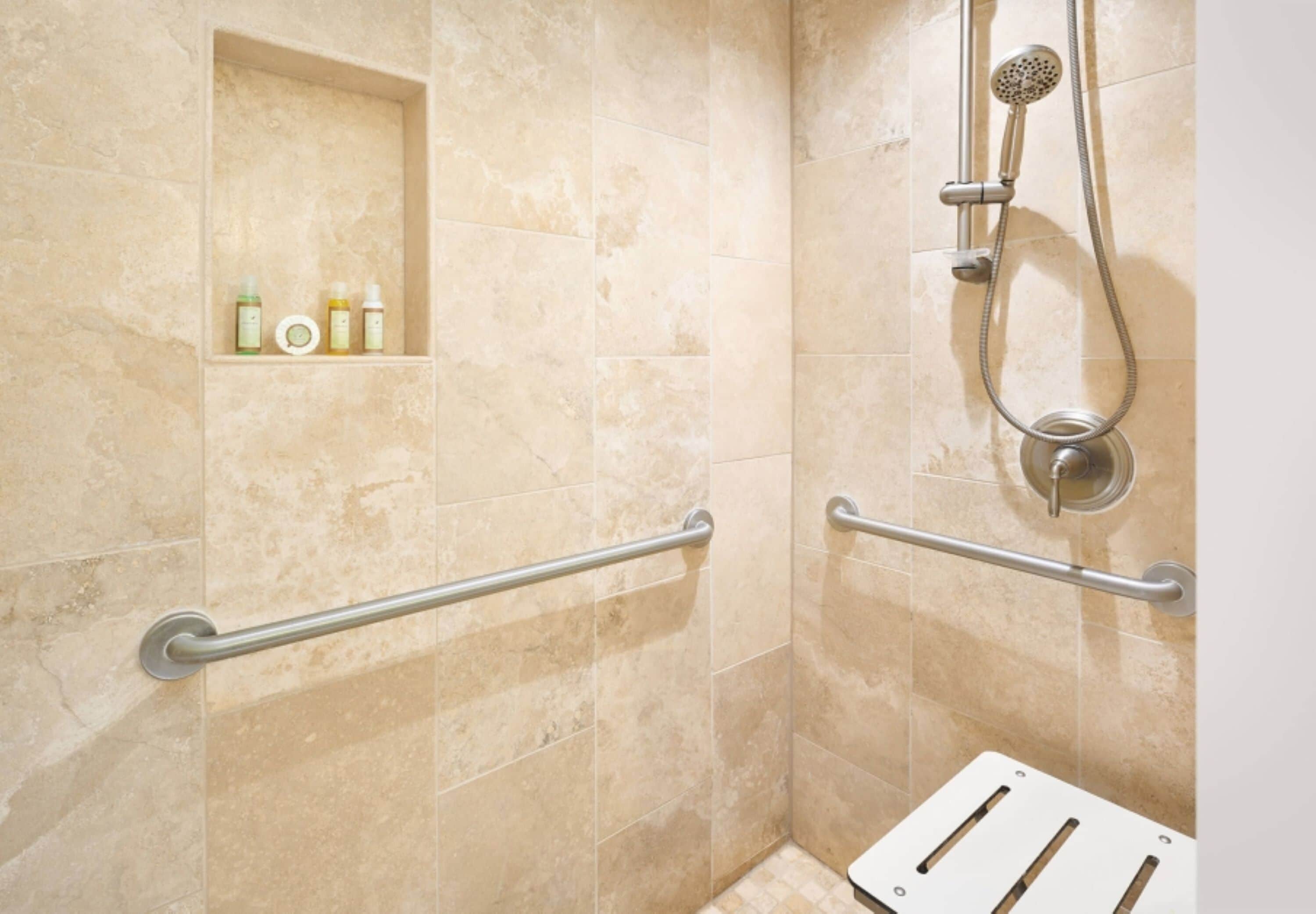 Un espace douche équipé de barres d’appui, d’un pommeau de douche et d’une étagère pour les articles de toilette.