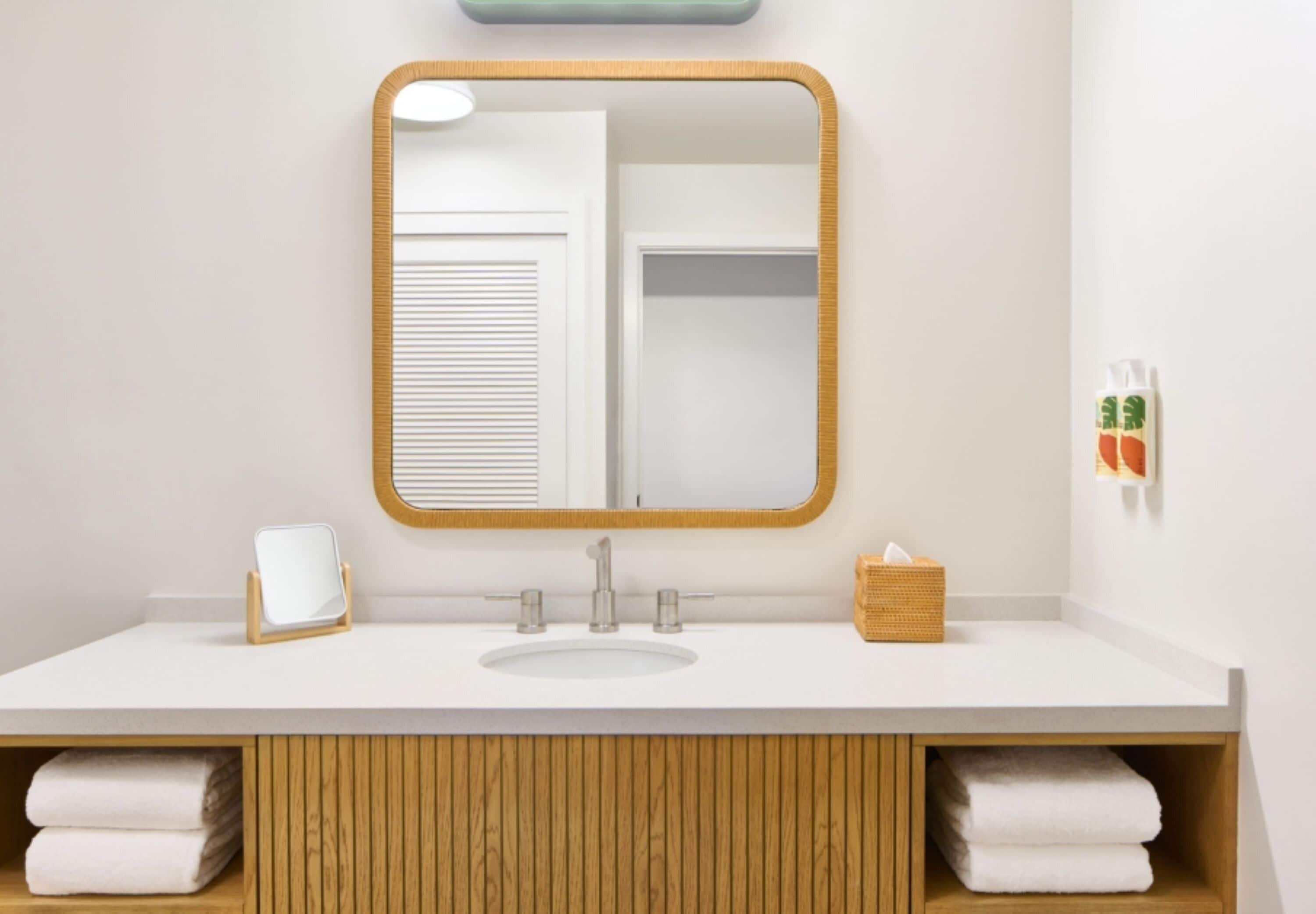 A bathroom with a white sink, a mirror with a wooden frame, a towel rack, and a basket.