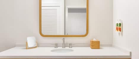 A bathroom with a white sink, a mirror with a wooden frame, a towel rack, and a basket.