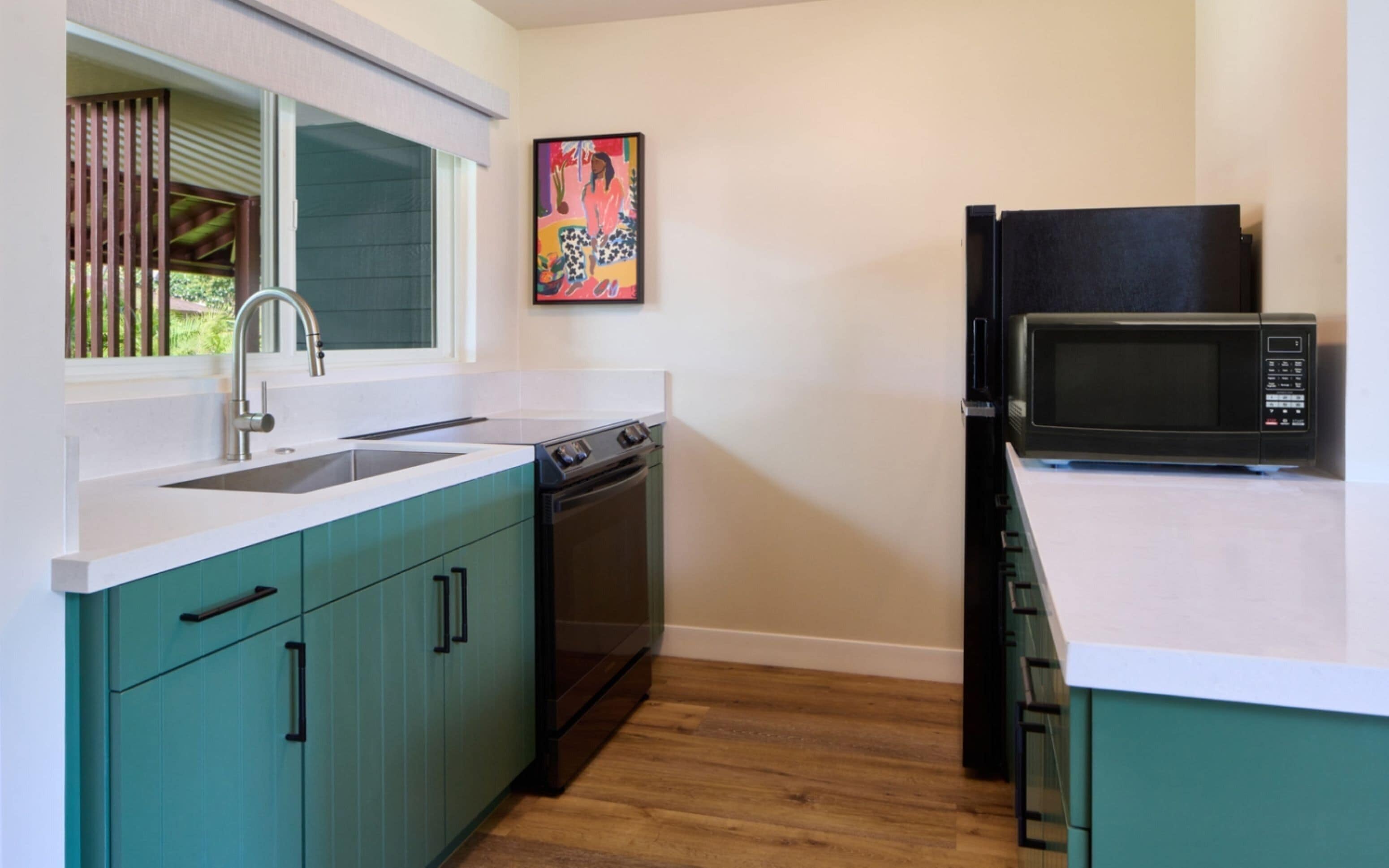 A kitchen with teal cabinets, a white countertop, a stainless steel sink, a dishwasher, a stove, and a black microwave.