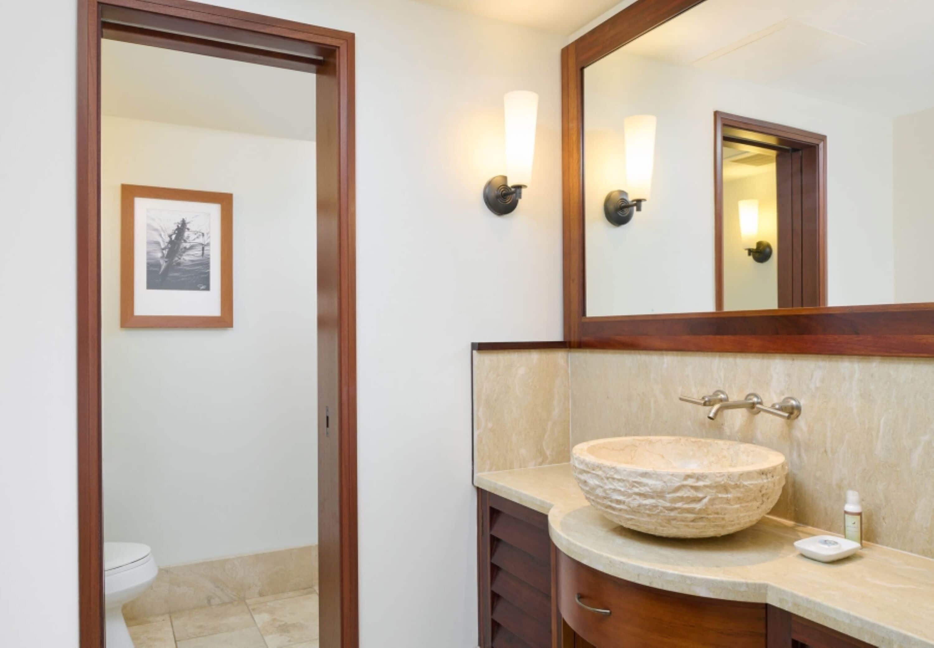A bathroom with a large mirror, a stone sink, and a framed picture on the wall.