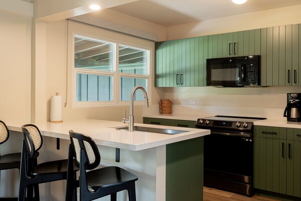 A modern kitchen with green cabinets, a black microwave, a stove, and a sink. - Royal Lahaina Resort & Bungalows (Lahaina)