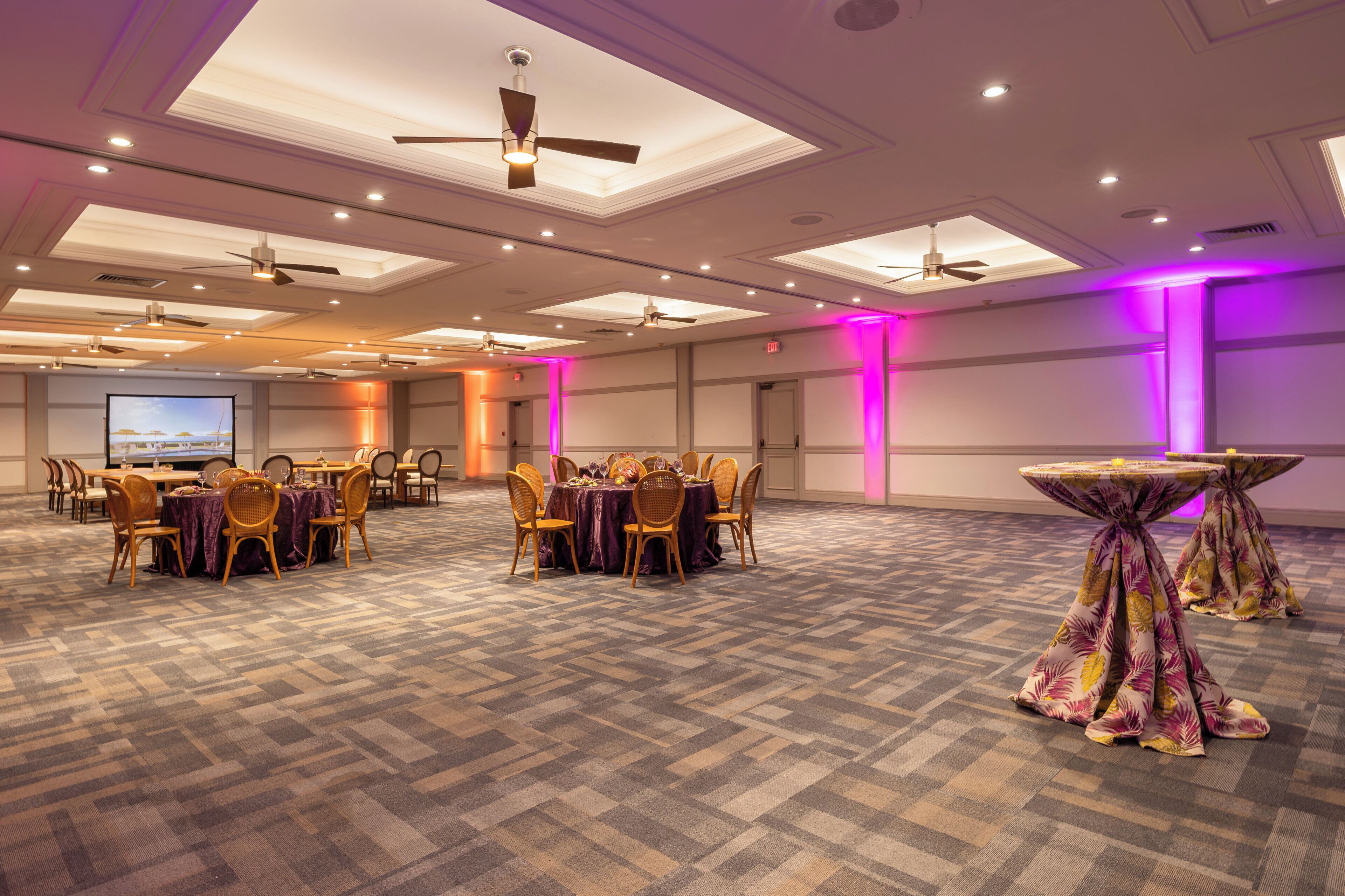 A conference room with multiple tables and chairs, ceiling fans, and recessed lighting.