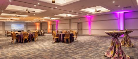 A conference room with multiple tables and chairs, ceiling fans, and recessed lighting.