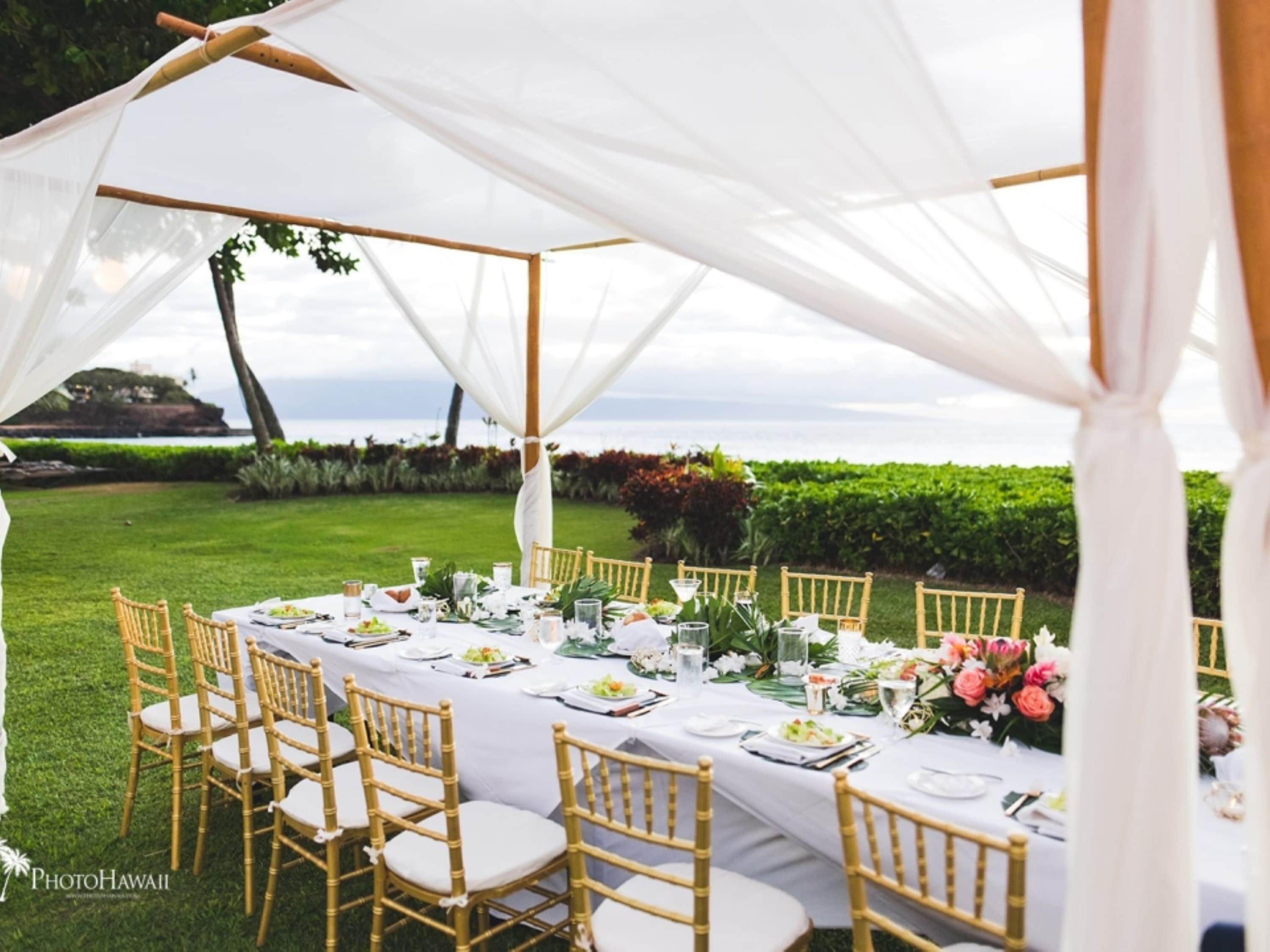 Una tenda da matrimonio all'aperto con tovaglia bianca, sedie dorate e centrotavola floreali.