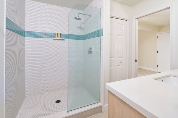 Une salle de bain moderne avec une douche à parois de verre, un lavabo blanc et une porte donnant sur une autre pièce.