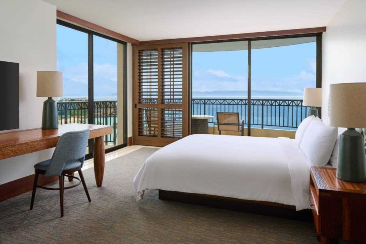 Habitación de hotel con una cama grande, un escritorio, una silla y vista al océano.