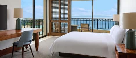 A hotel room with a large bed, a desk, a chair, and a view of the ocean.