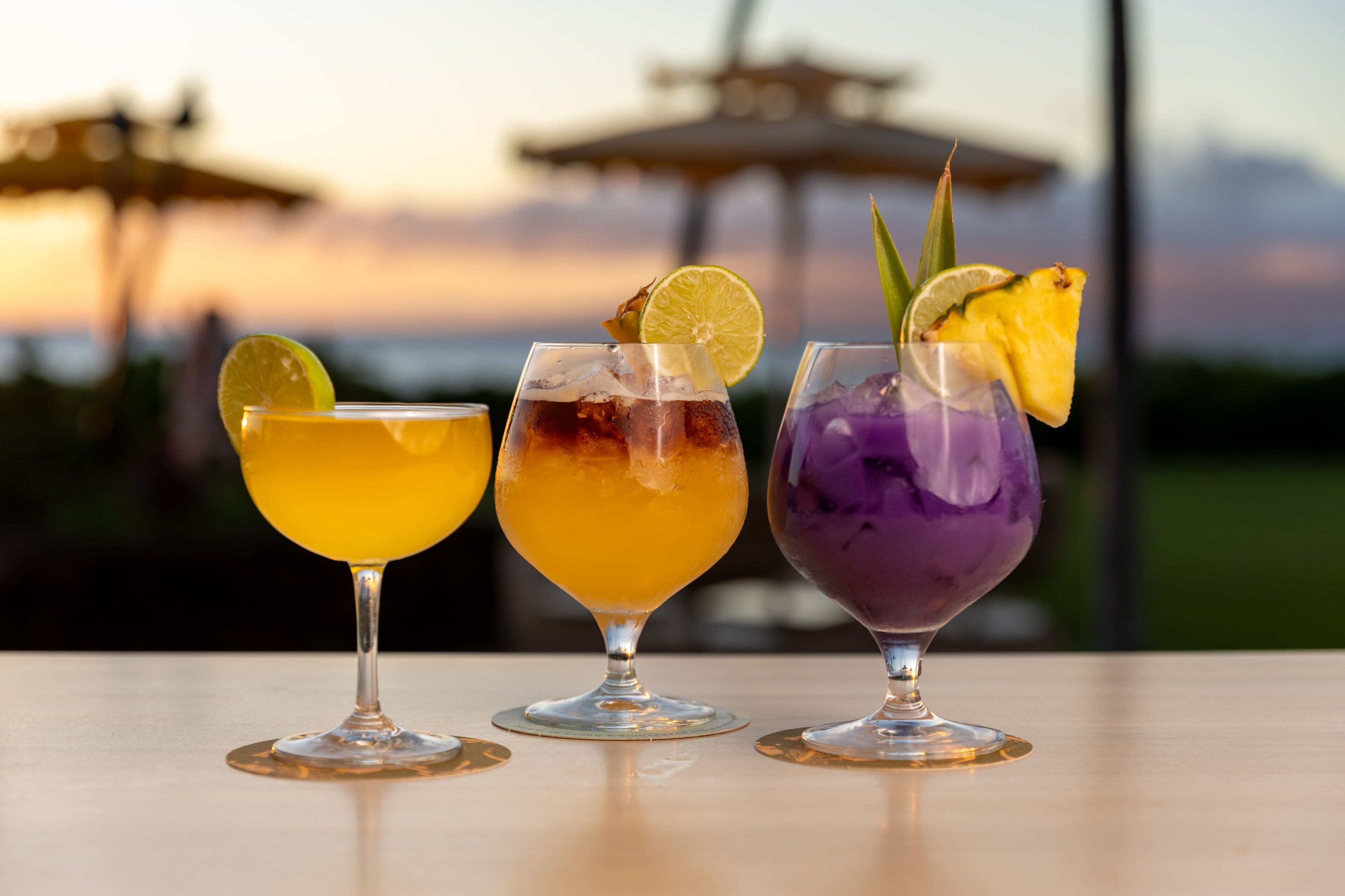 Tres cócteles sobre una mesa, con vista al atardecer.