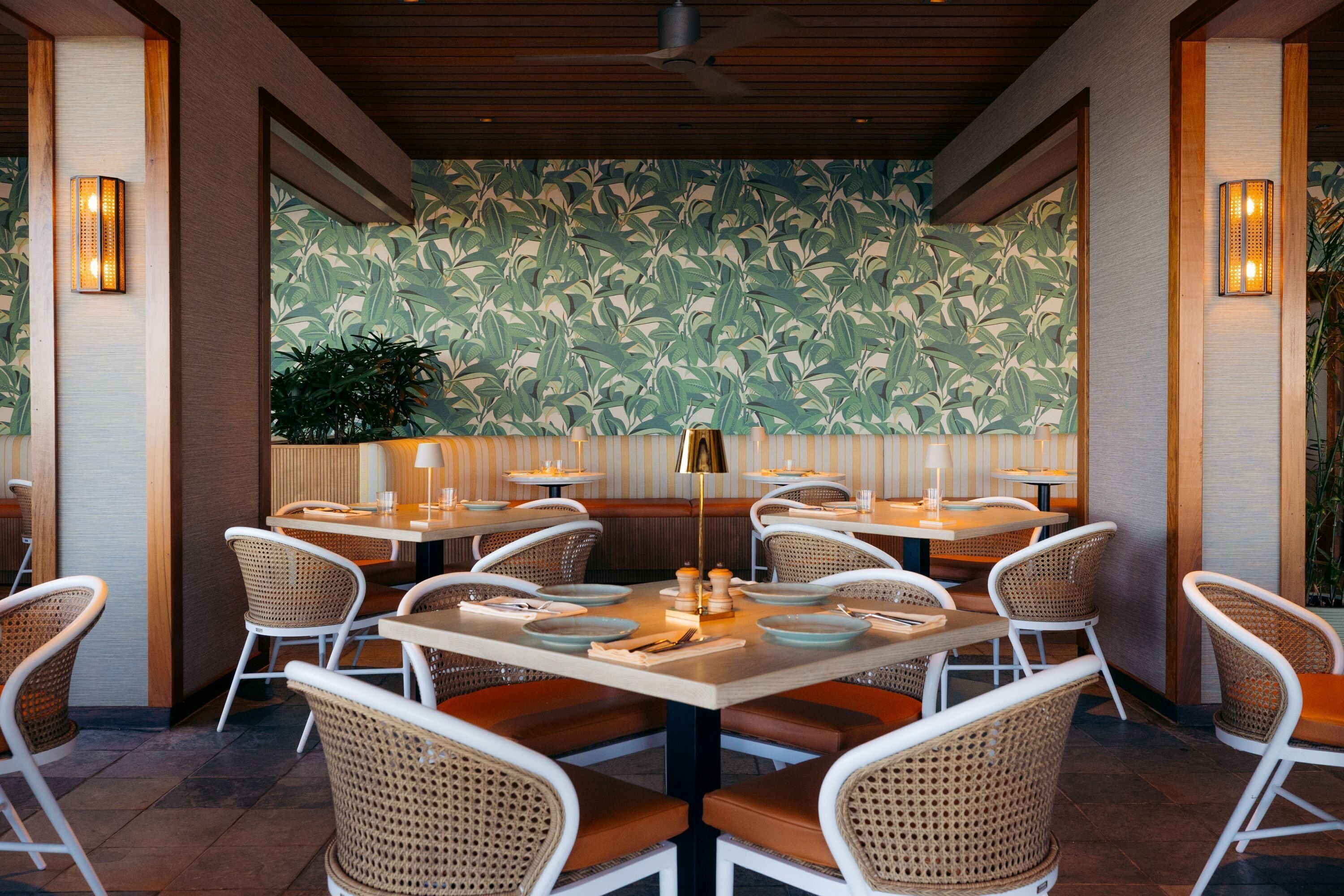 An indoor dining area with round tables, wicker chairs, and a patterned wall.