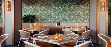An indoor dining area with round tables, wicker chairs, and a patterned wall.