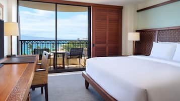 Habitación de hotel con una cama grande, un escritorio y una silla. Tiene un balcón con vistas al océano.