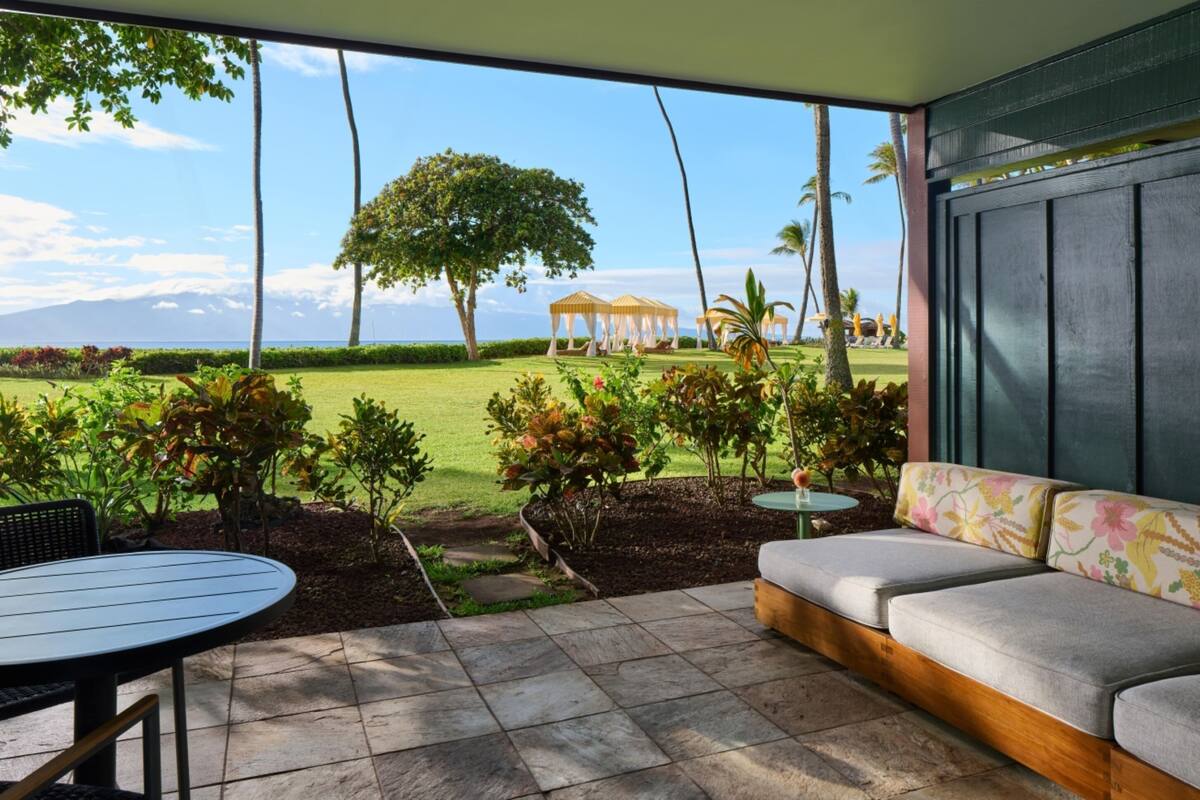 Un patio con un área de estar con cojines, una mesa redonda y vistas a un campo de golf con un árbol y sombrillas.