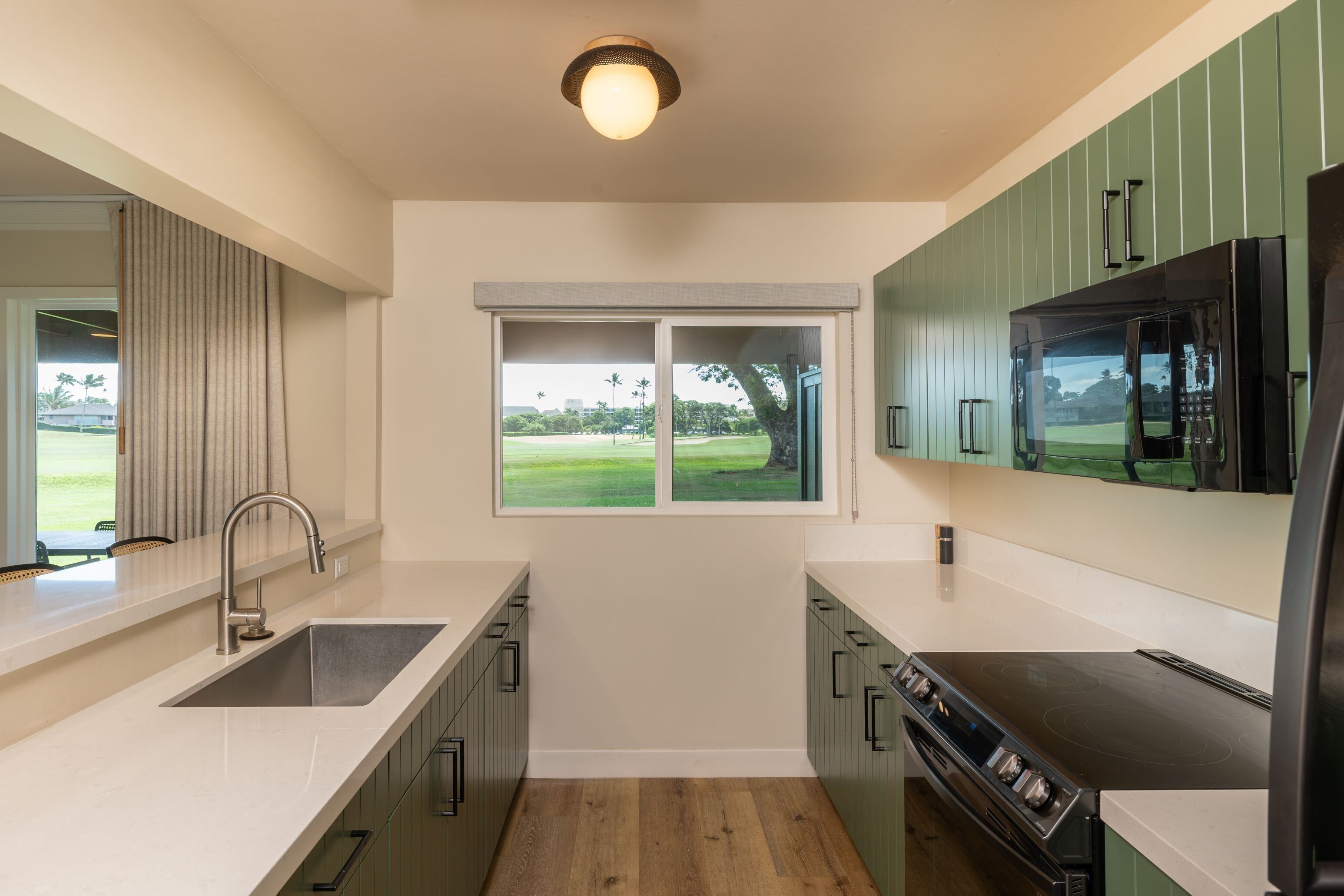 A modern kitchen with a large window, a built-in stove, and green cabinetry.