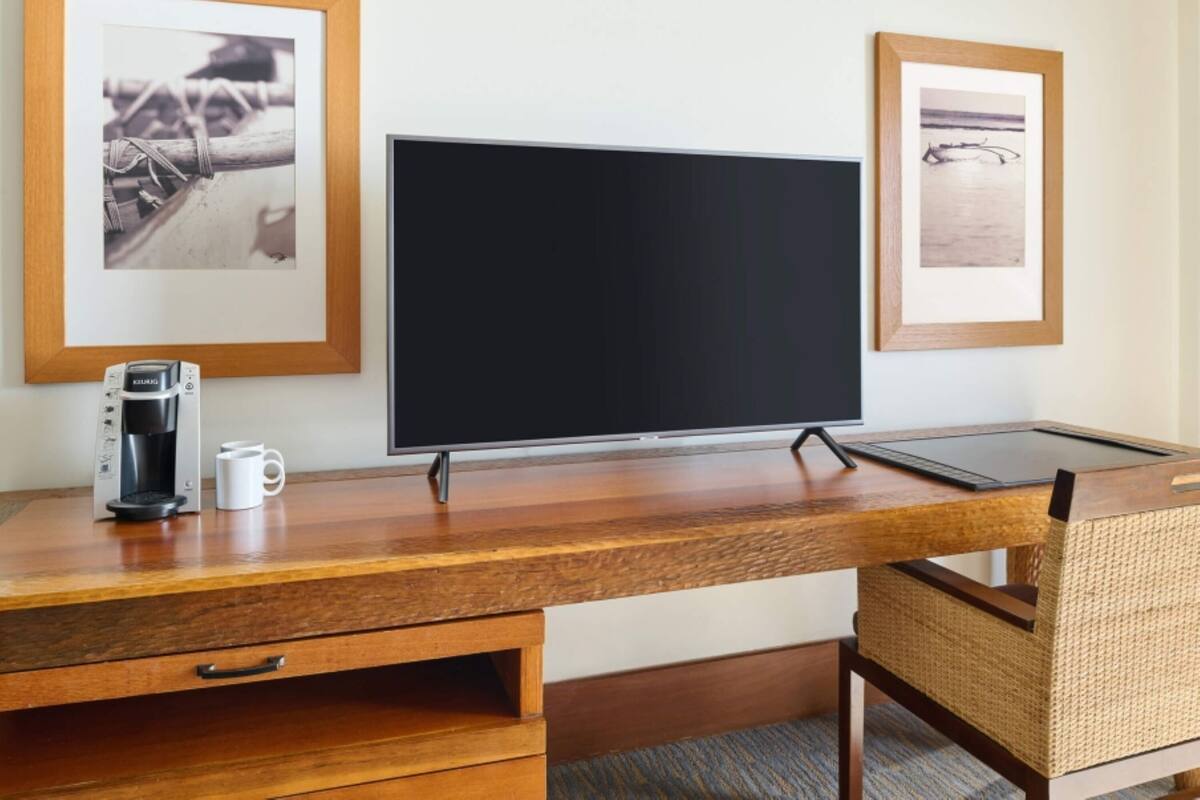 Un escritorio de madera con una cafetera y una taza, un televisor de pantalla plana y dos cuadros en la pared.