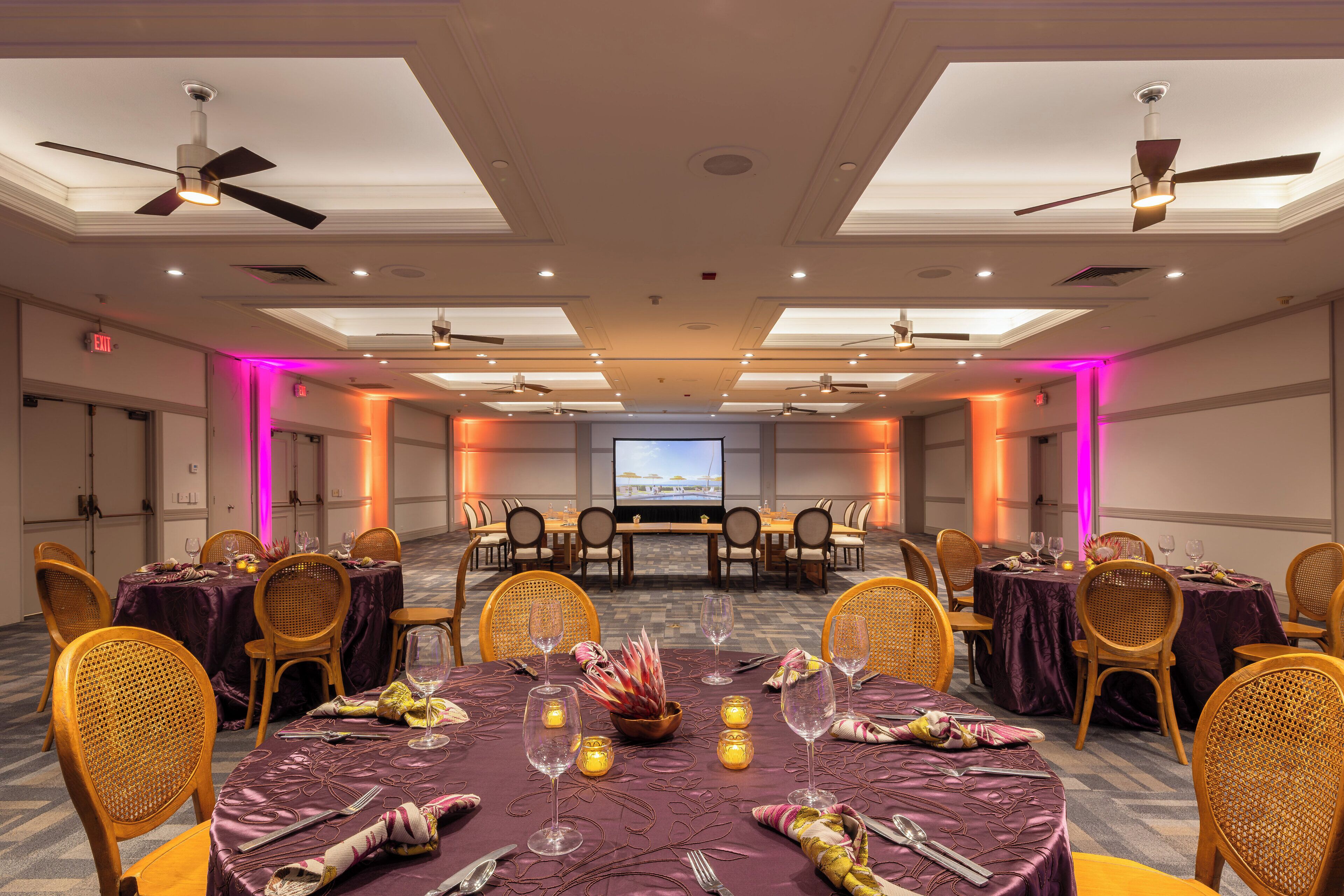 A conference room with round tables, chairs, and a large screen at the front.