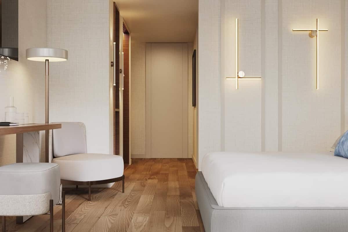 Una habitación de hotel moderna con suelo de madera, una cama, un escritorio con silla y un armario.