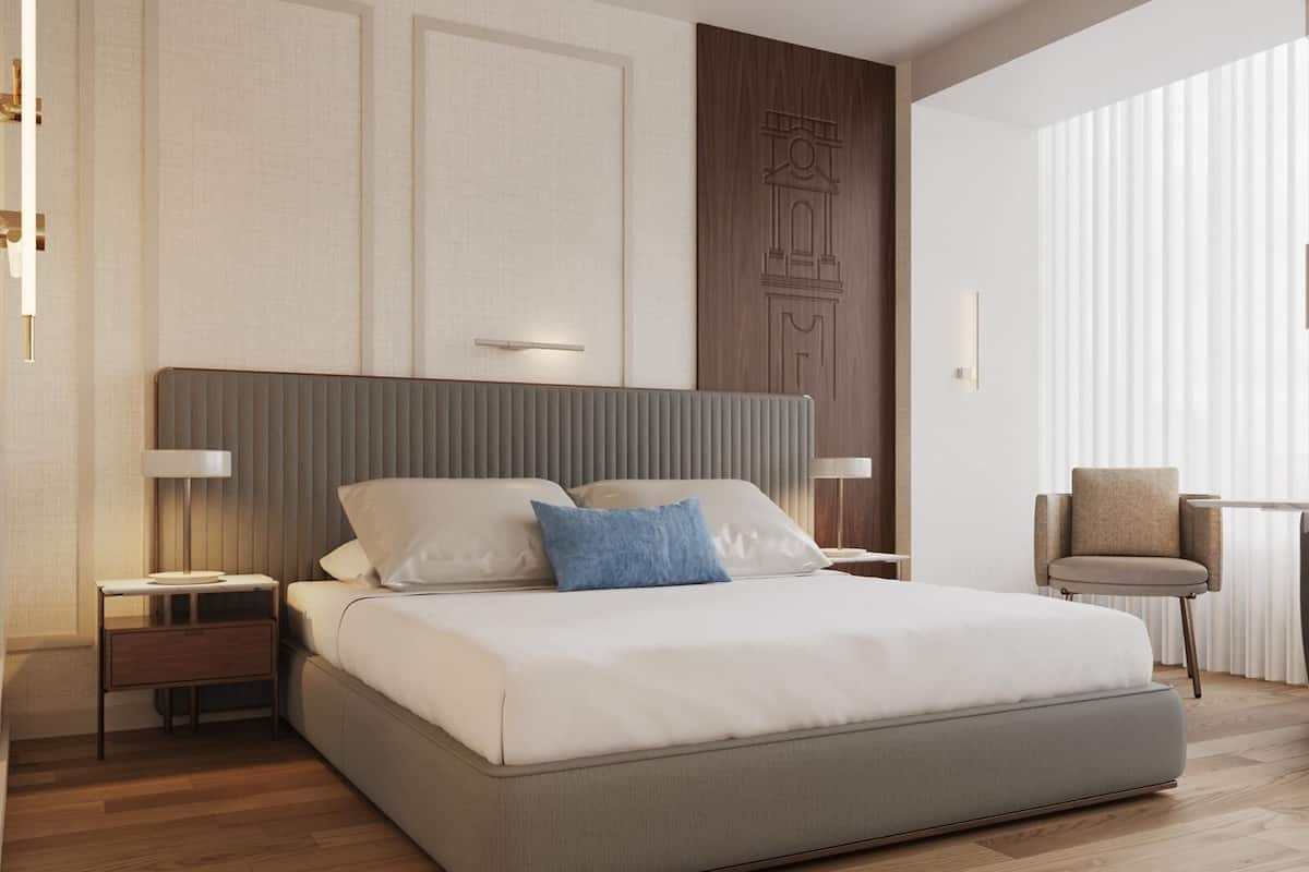 Una habitación de hotel moderna con una cama grande, un cabecero de madera, una mesita de noche, una silla y un ventanal con persianas.
