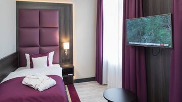 Una habitación de hotel con una cama grande, un televisor de pantalla plana en la pared, una mesita de noche y una pequeña mesa redonda.