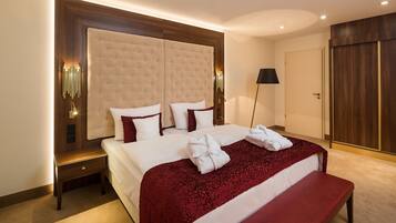 Habitación de hotel con una cama grande, cabecera de madera, un banco, una mesita de noche y un armario.