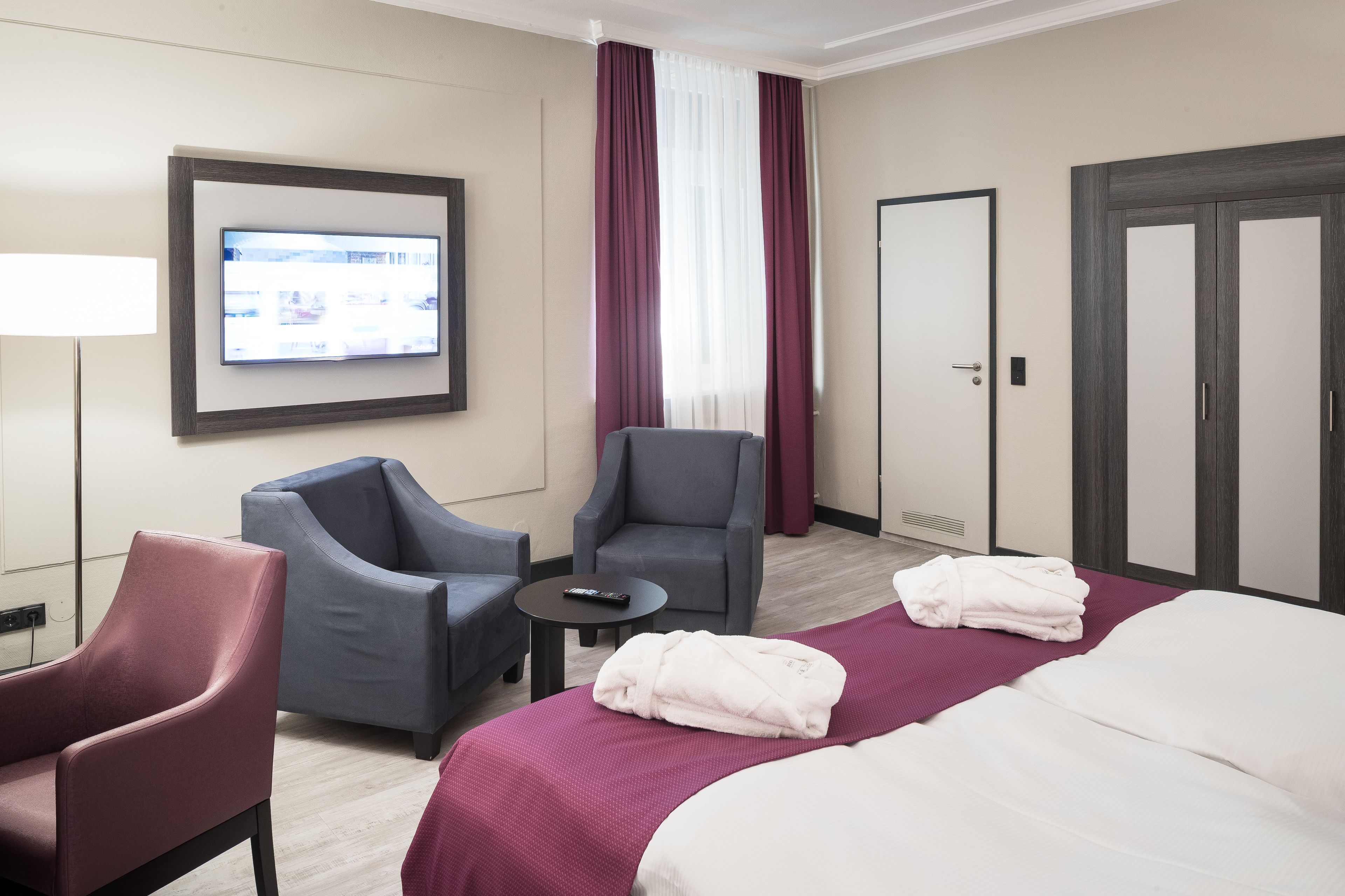 A hotel room with a bed, two armchairs, a TV, and a wardrobe.