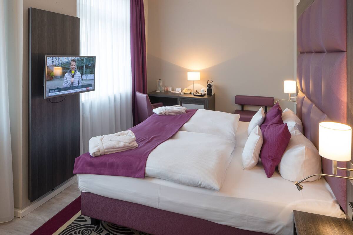 A hotel room with a large bed, a desk, a television, and a nightstand.