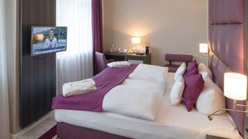 A hotel room with a large bed, a desk, a television, and a nightstand.