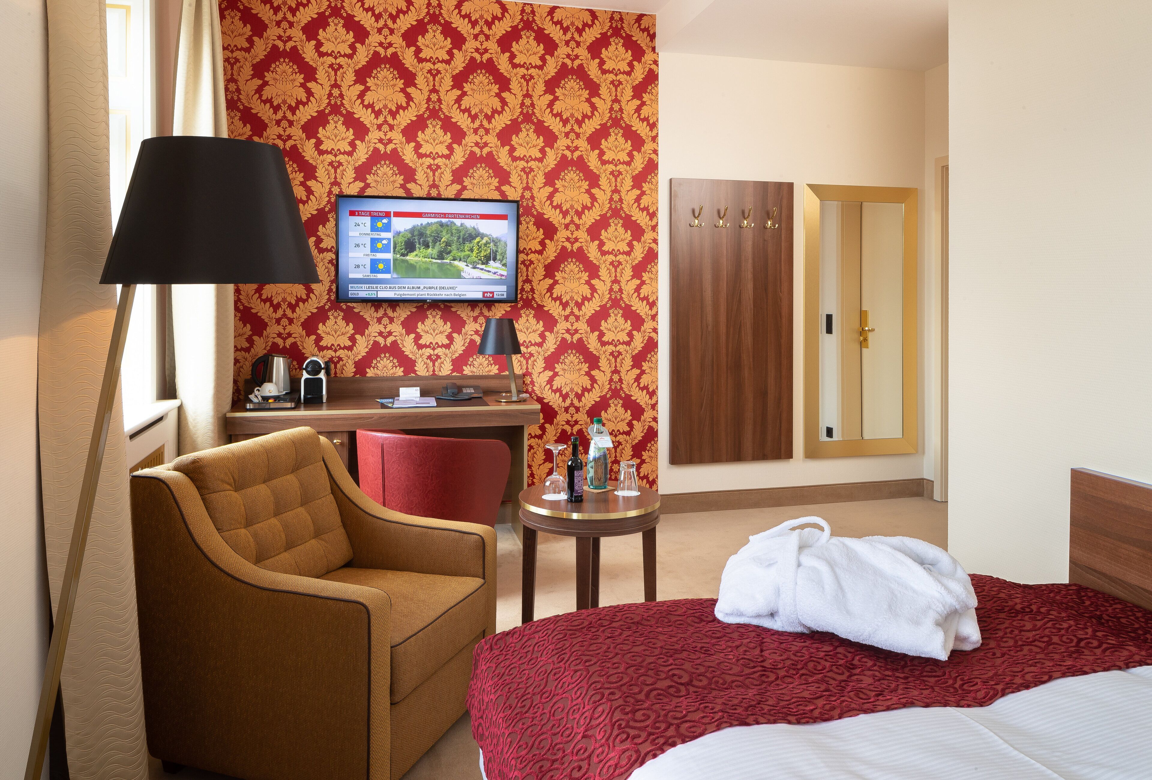 A hotel room with a bed, a desk, a chair, a TV, and a wardrobe.