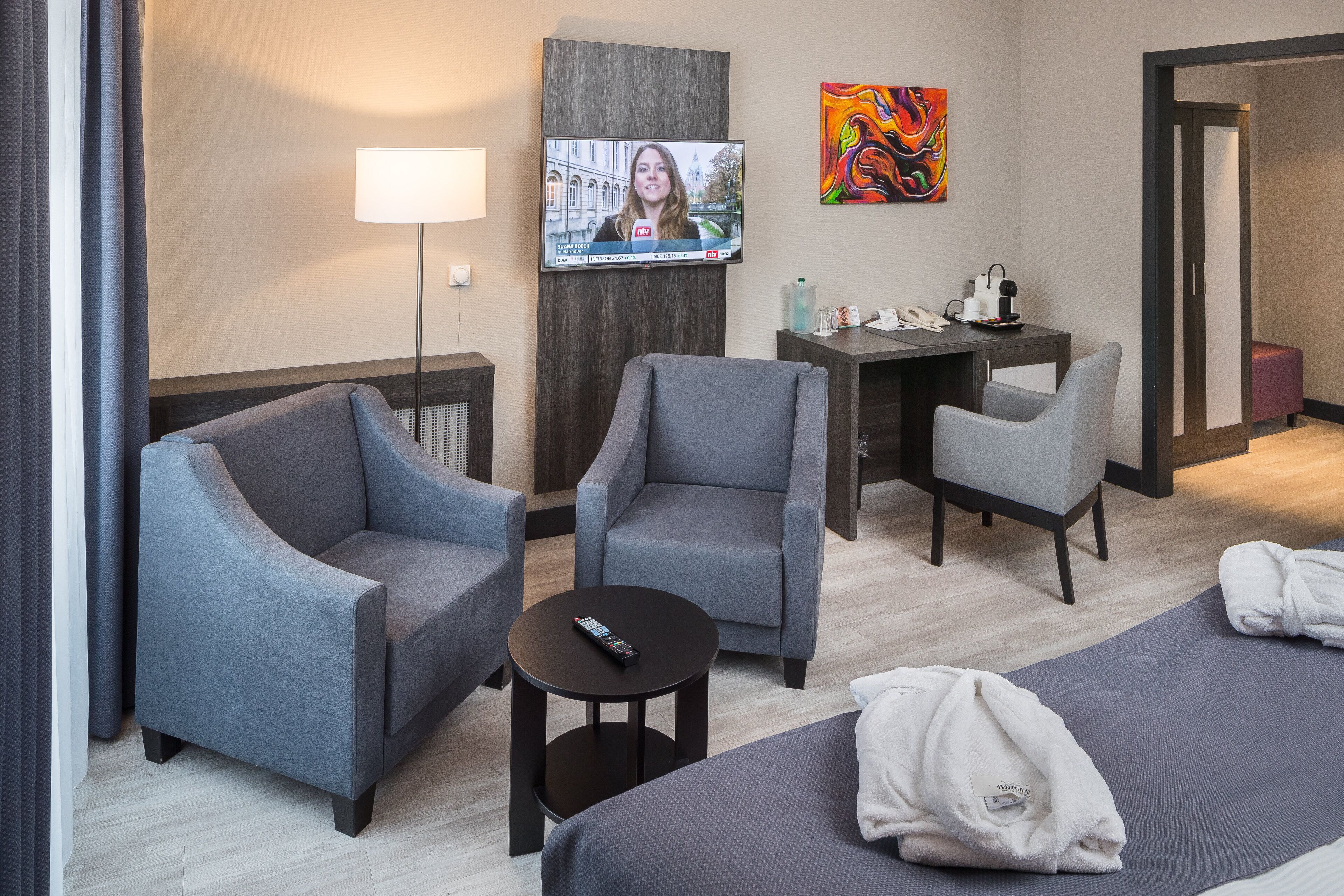 Hotelkamer met een bed, twee fauteuils, een bureau, een televisie en een schilderij aan de muur.
