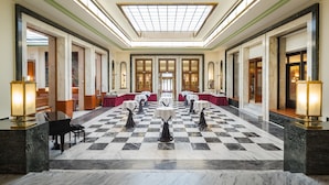 A spacious lobby with a checkered marble floor, a grand piano, and tables set for dining. - Hotel Chemnitzer Hof (Chemnitz)